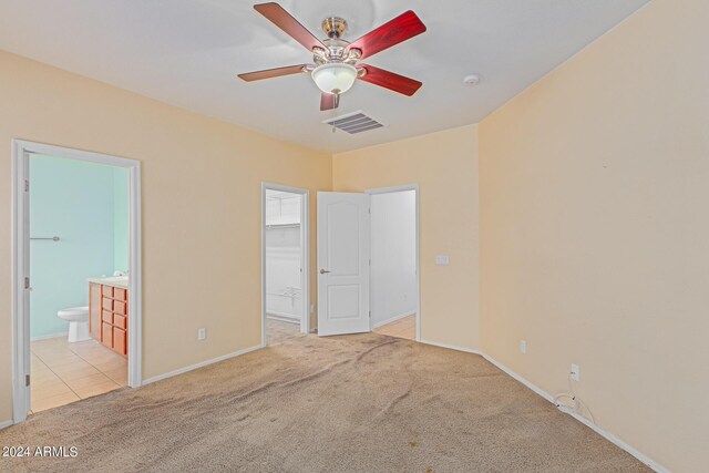 unfurnished bedroom featuring light carpet, a closet, connected bathroom, and a walk in closet