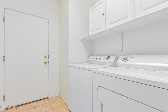 laundry area with light tile patterned floors, washing machine and clothes dryer, and cabinets