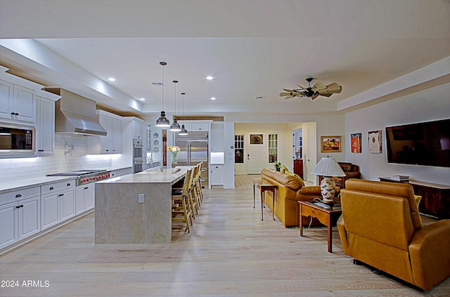 kitchen featuring pendant lighting, built in appliances, a breakfast bar area, wall chimney exhaust hood, and white cabinetry