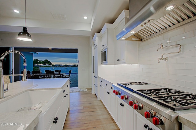 kitchen featuring decorative light fixtures, backsplash, light wood-type flooring, and wall chimney range hood