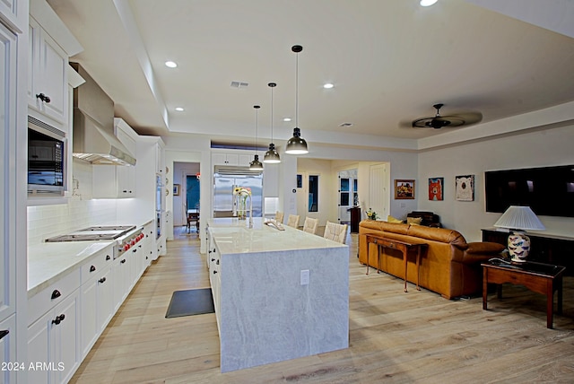 kitchen featuring built in appliances, ceiling fan, pendant lighting, white cabinets, and light wood-type flooring