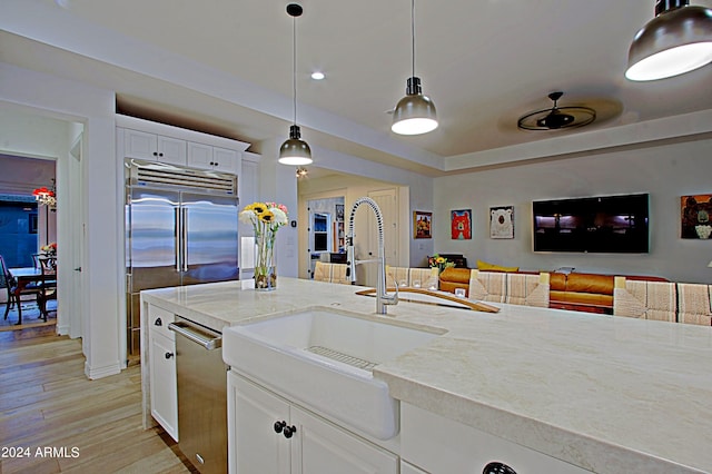 kitchen featuring decorative light fixtures, appliances with stainless steel finishes, light hardwood / wood-style floors, white cabinetry, and sink