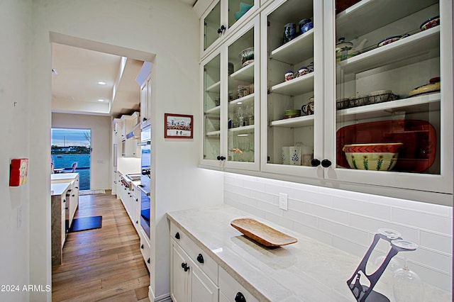 bar with light wood-type flooring, stainless steel oven, light stone countertops, and white cabinetry