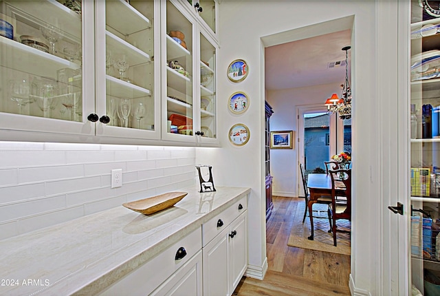 kitchen featuring an inviting chandelier, light stone counters, white cabinetry, light wood-type flooring, and backsplash