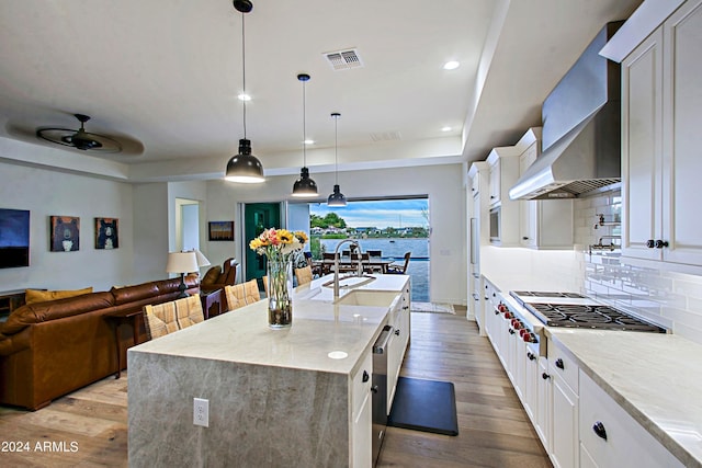 kitchen featuring white cabinetry, light wood-type flooring, light stone countertops, ceiling fan, and wall chimney range hood