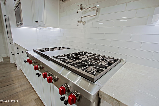 kitchen featuring range, white cabinetry, backsplash, stainless steel microwave, and light hardwood / wood-style floors