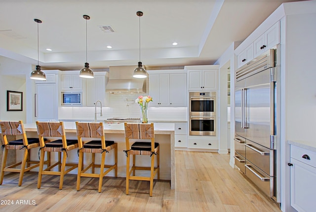 kitchen with decorative light fixtures, white cabinetry, built in appliances, custom range hood, and light wood-type flooring