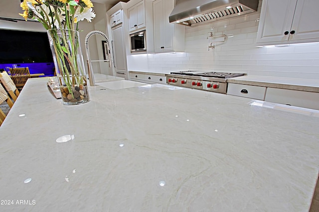 kitchen featuring light stone countertops, stainless steel appliances, white cabinetry, and wall chimney range hood