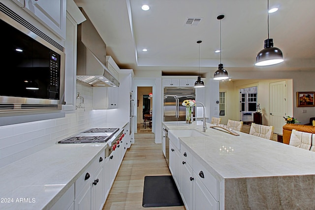 kitchen featuring hanging light fixtures, white cabinetry, backsplash, wall chimney exhaust hood, and built in appliances