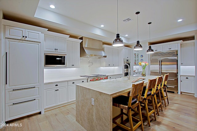 kitchen with wall chimney range hood, backsplash, white cabinets, and light wood-type flooring