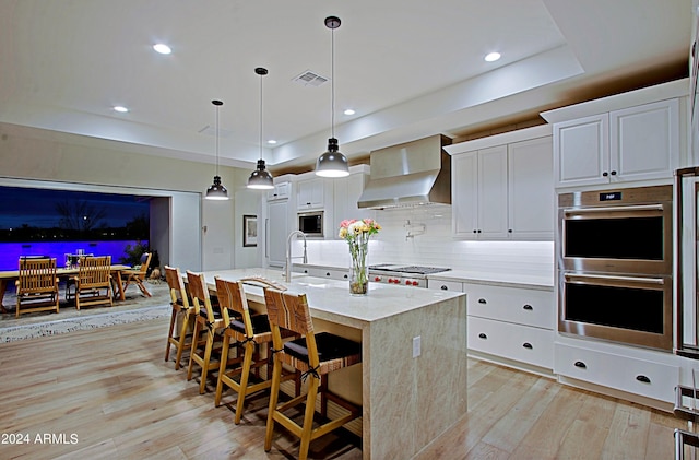 kitchen with white cabinets, pendant lighting, stainless steel appliances, and wall chimney range hood