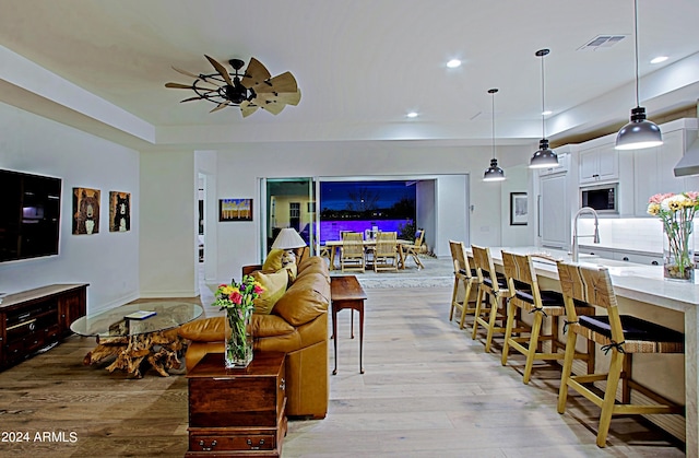 living room with ceiling fan, sink, light wood-type flooring, and a tray ceiling