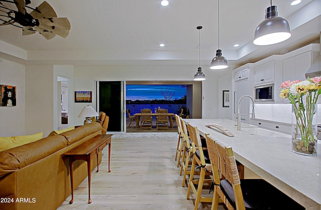 kitchen with ceiling fan, hanging light fixtures, stainless steel microwave, white cabinets, and light wood-type flooring