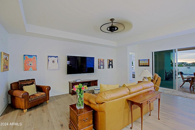 living room featuring a raised ceiling, light hardwood / wood-style floors, ceiling fan, and a water view