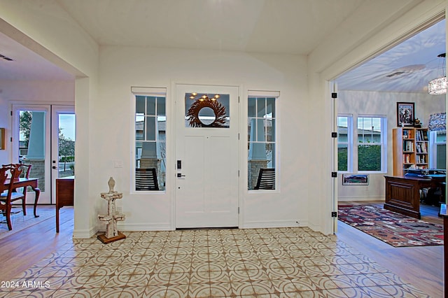 foyer entrance with french doors, a notable chandelier, and light wood-type flooring