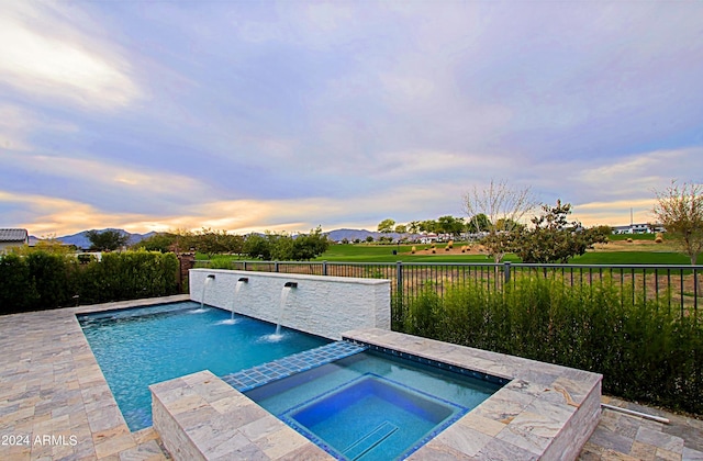 pool at dusk with an in ground hot tub and pool water feature