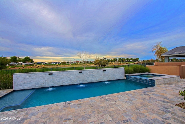 pool at dusk with an in ground hot tub, pool water feature, and a patio area