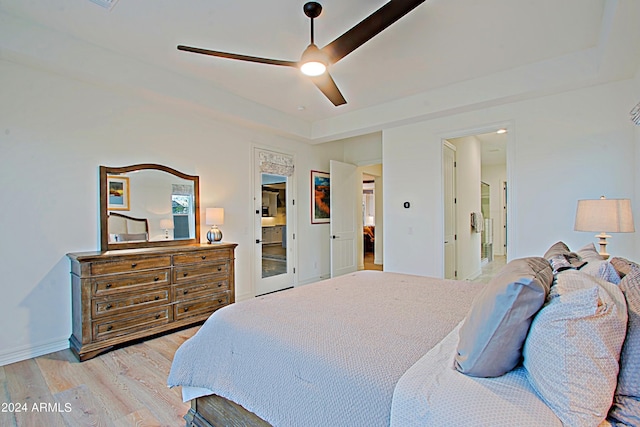 bedroom featuring a raised ceiling, light hardwood / wood-style floors, ceiling fan, and connected bathroom