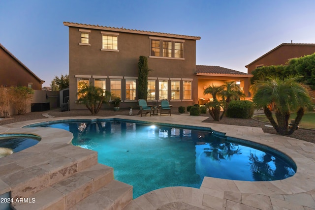 pool at dusk with a patio and an in ground hot tub