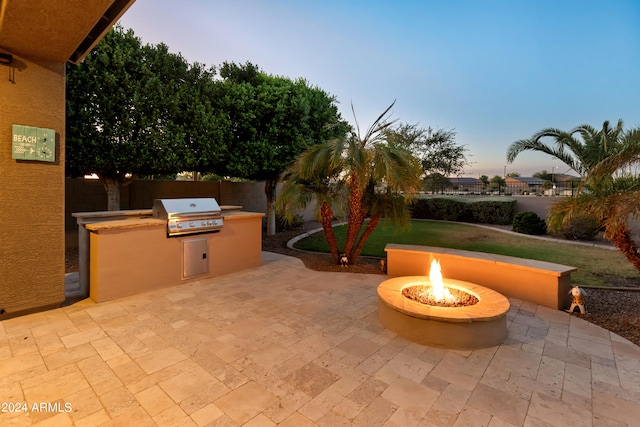 patio terrace at dusk featuring grilling area, an outdoor kitchen, a yard, and an outdoor fire pit