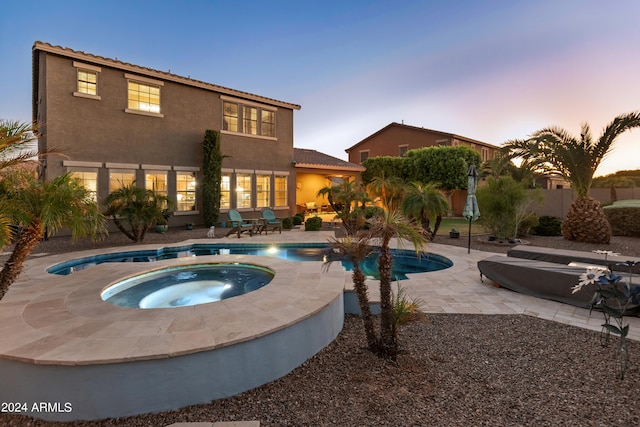 pool at dusk featuring an in ground hot tub and a patio area