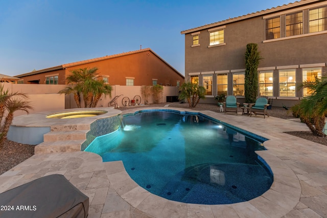 pool at dusk with a patio and an in ground hot tub