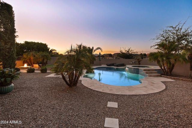 pool at dusk with a patio and an in ground hot tub