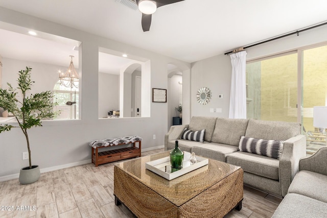 living room with baseboards, recessed lighting, ceiling fan with notable chandelier, light wood-style floors, and arched walkways