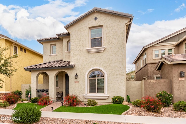 mediterranean / spanish home with stucco siding, fence, and a tiled roof