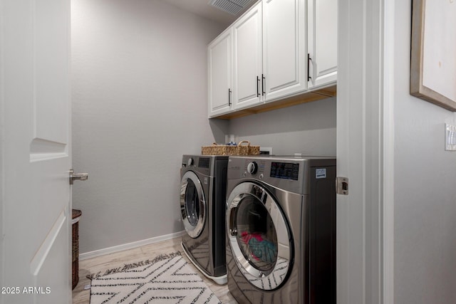 washroom with light wood finished floors, baseboards, cabinet space, and washer and clothes dryer