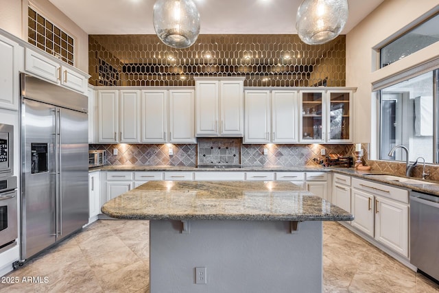 kitchen featuring a kitchen breakfast bar, built in appliances, decorative light fixtures, and sink