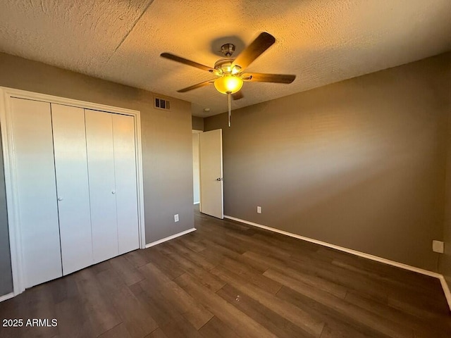 unfurnished bedroom with a textured ceiling, visible vents, baseboards, a closet, and dark wood-style floors