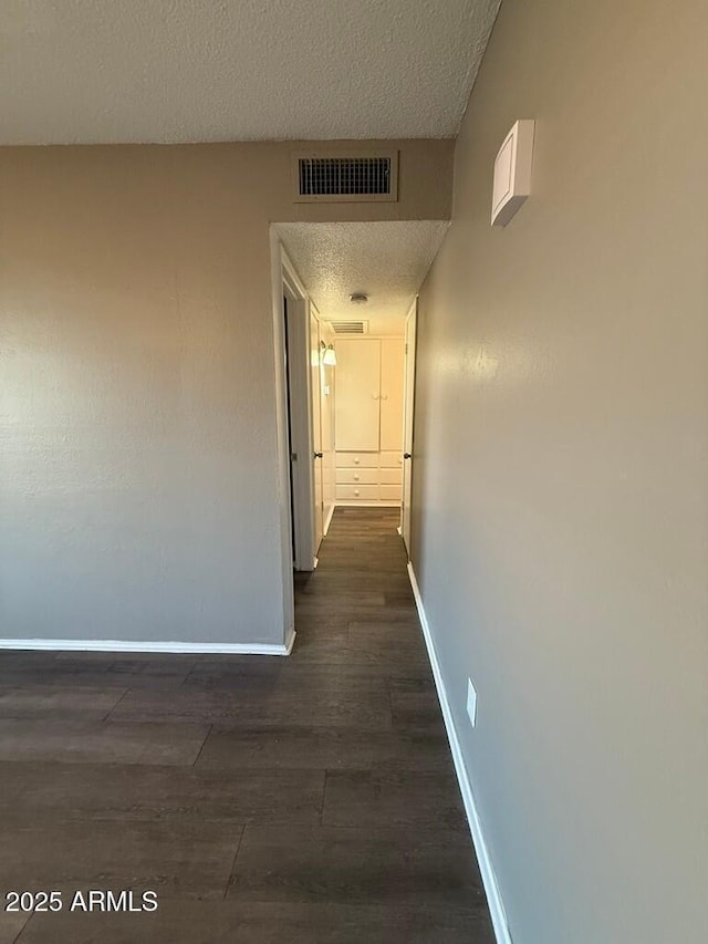 corridor featuring a textured ceiling, dark wood-style floors, visible vents, and baseboards