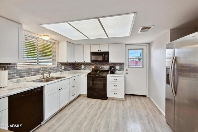 kitchen with light wood finished floors, a sink, white cabinets, black appliances, and backsplash
