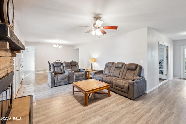 living room with ceiling fan with notable chandelier, baseboards, visible vents, and light wood-style floors