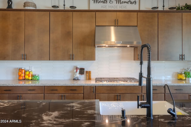 kitchen featuring wall chimney range hood, decorative backsplash, stainless steel gas stovetop, and light stone counters