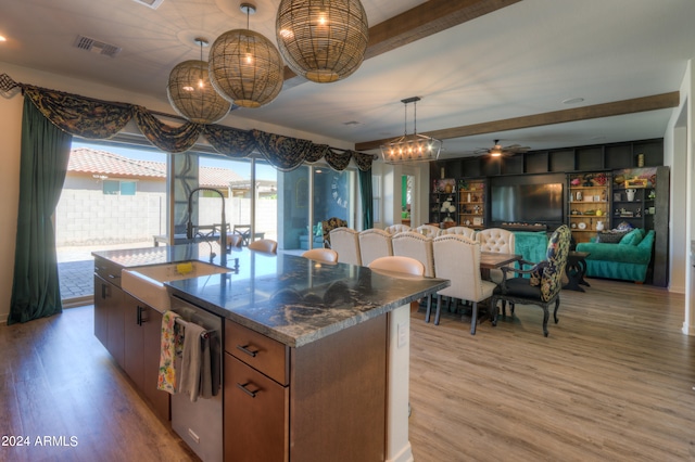 kitchen with a kitchen island with sink, dark stone counters, stainless steel dishwasher, light hardwood / wood-style floors, and ceiling fan