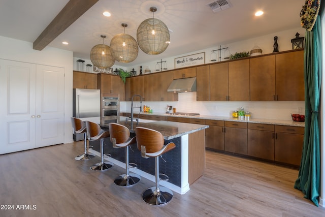 kitchen featuring a kitchen island with sink, hanging light fixtures, and light wood-type flooring