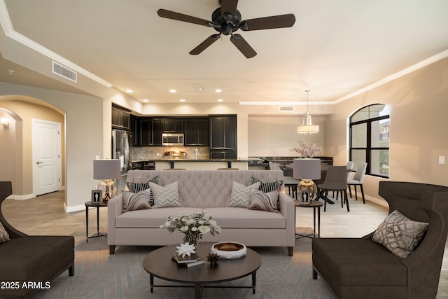 living room featuring visible vents, arched walkways, baseboards, and ornamental molding