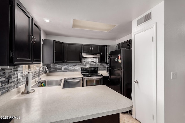 kitchen with stainless steel appliances, a sink, dark cabinetry, under cabinet range hood, and light countertops