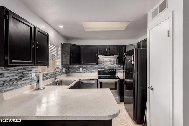 kitchen featuring appliances with stainless steel finishes, dark cabinetry, a sink, under cabinet range hood, and light countertops