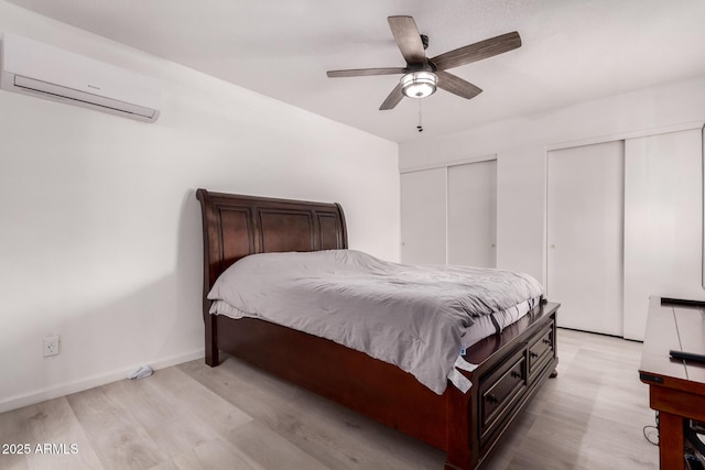 bedroom featuring an AC wall unit, two closets, light wood-style flooring, ceiling fan, and baseboards