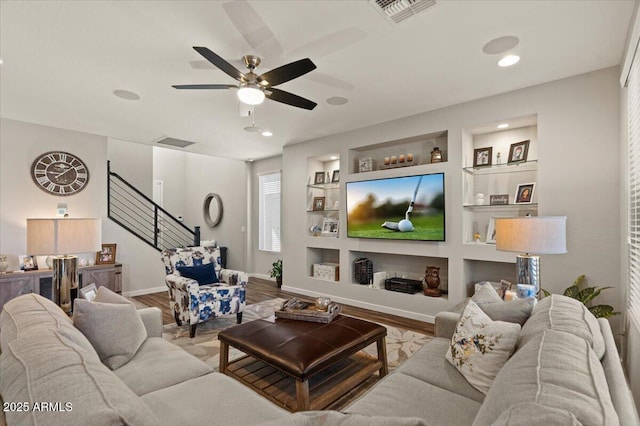 living room with built in features, a ceiling fan, stairs, wood finished floors, and recessed lighting