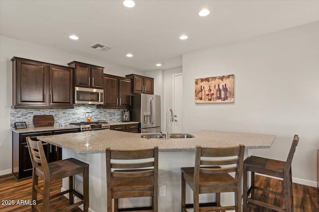 kitchen with appliances with stainless steel finishes, a sink, a breakfast bar, dark brown cabinetry, and dark wood-type flooring