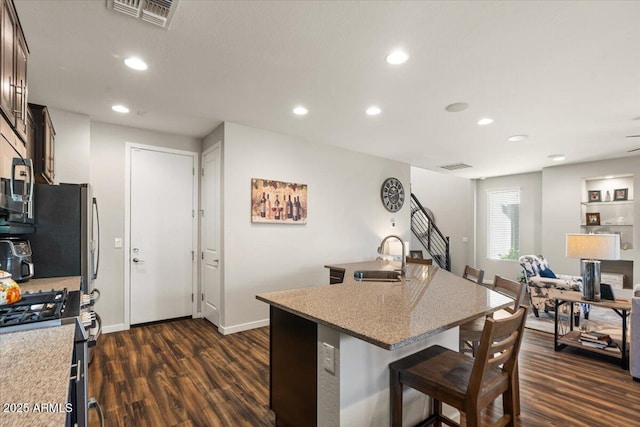 kitchen with a sink, gas stove, a breakfast bar, dark wood-style floors, and a center island with sink