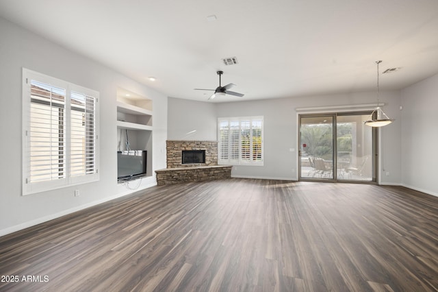 unfurnished living room featuring ceiling fan, a stone fireplace, dark hardwood / wood-style flooring, and built in shelves