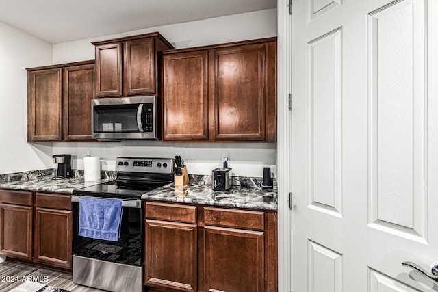 kitchen with appliances with stainless steel finishes, dark brown cabinetry, dark wood-type flooring, and dark stone counters