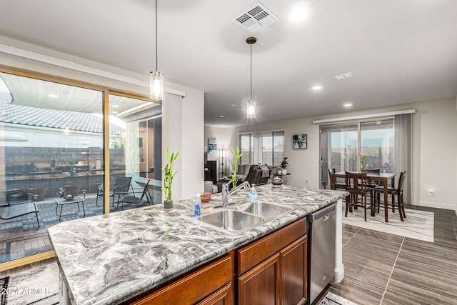 kitchen with light stone counters, sink, decorative light fixtures, dishwasher, and an island with sink