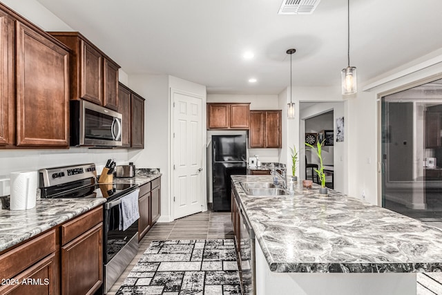 kitchen with hanging light fixtures, a kitchen island with sink, sink, and appliances with stainless steel finishes