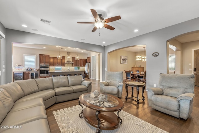 living room featuring a wealth of natural light, dark hardwood / wood-style floors, beverage cooler, and ceiling fan with notable chandelier